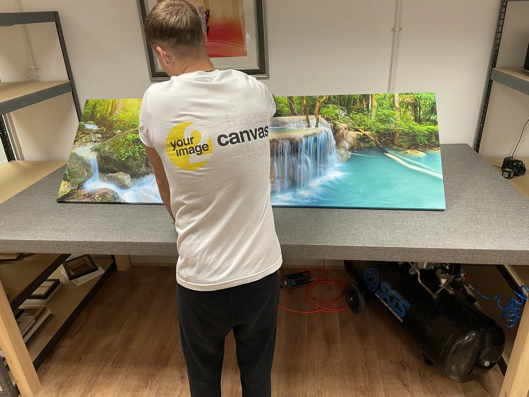 A printmaker carrying a large waterfall canvas across a finishing bench