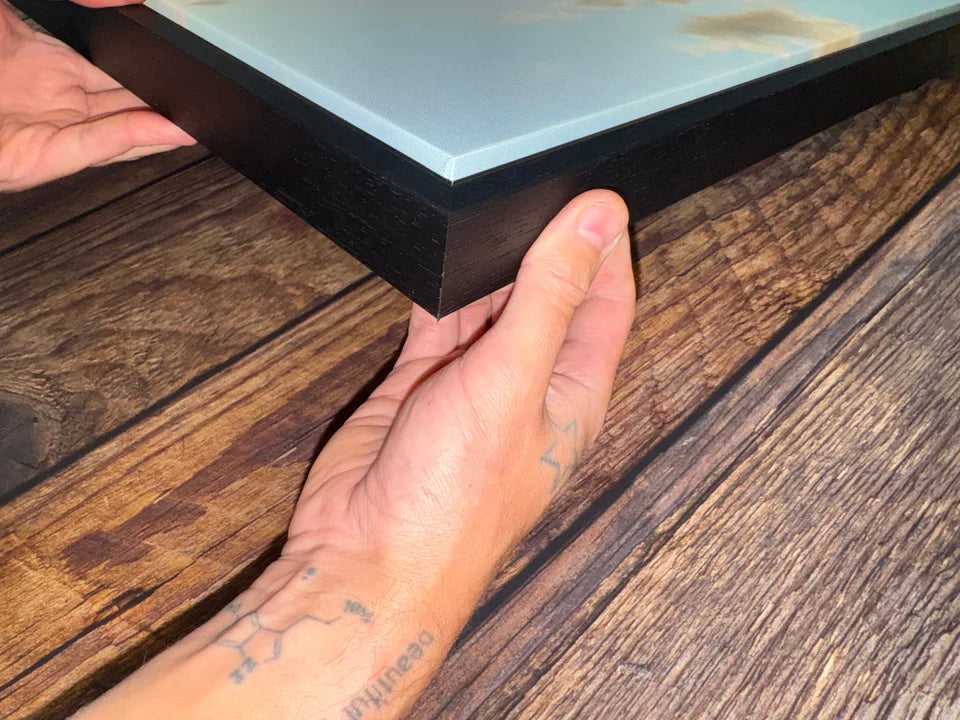 Hands holding the corner of a real photo canvas in a black floating frame, showing the depth and shadow gap.