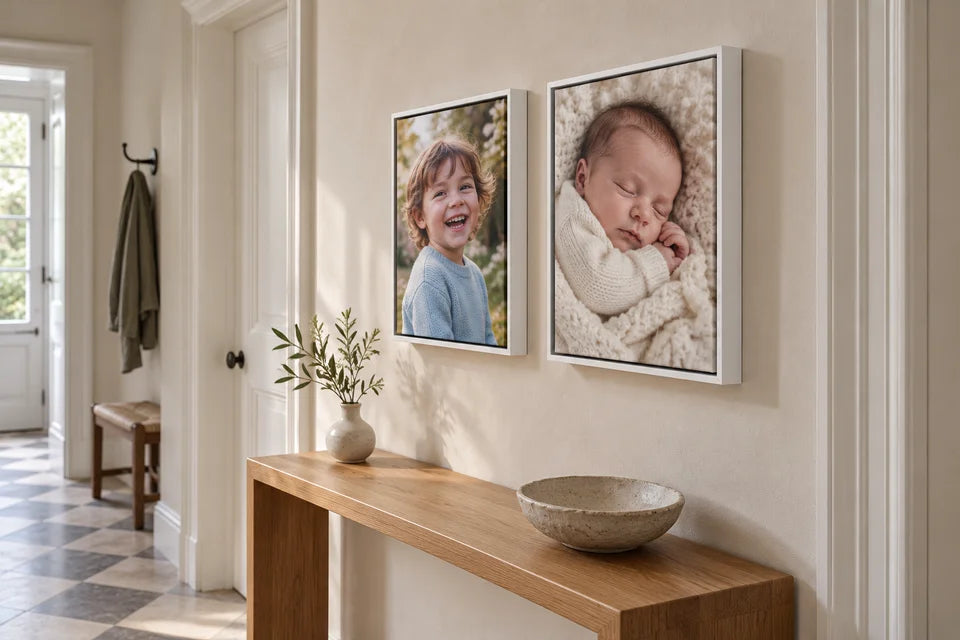 Two small child and newborn photo canvases in white floating frames above a narrow hallway console.