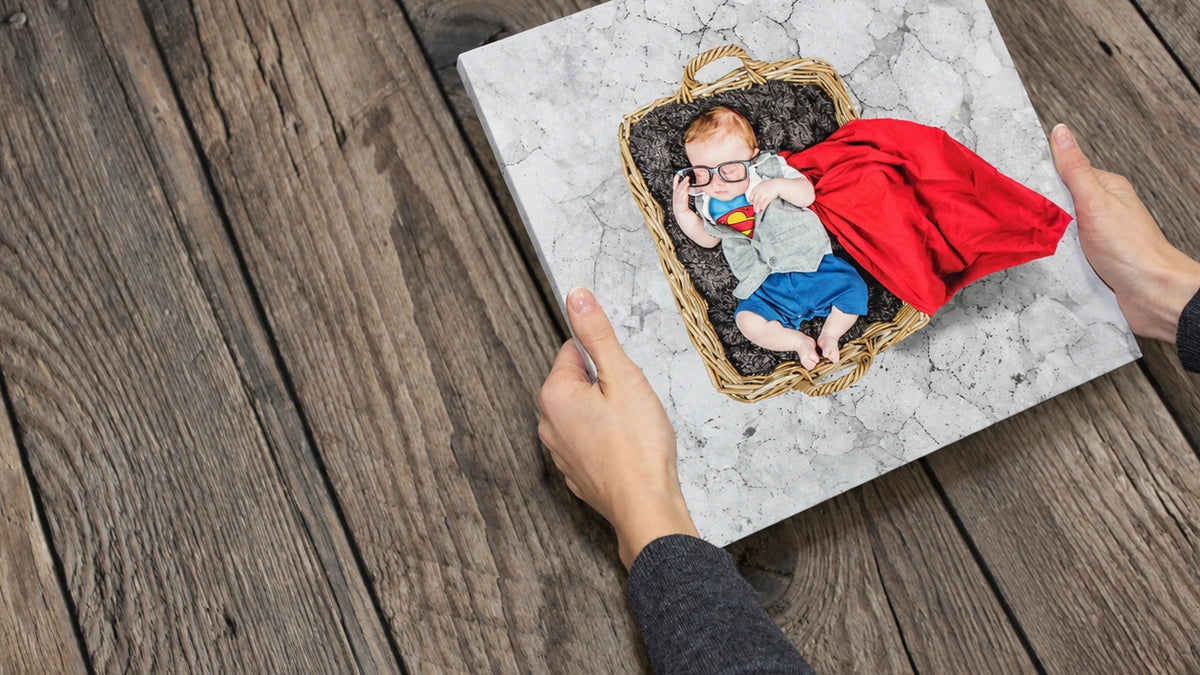 A real baby photograph printed on stretched canvas, held above a wooden floor.