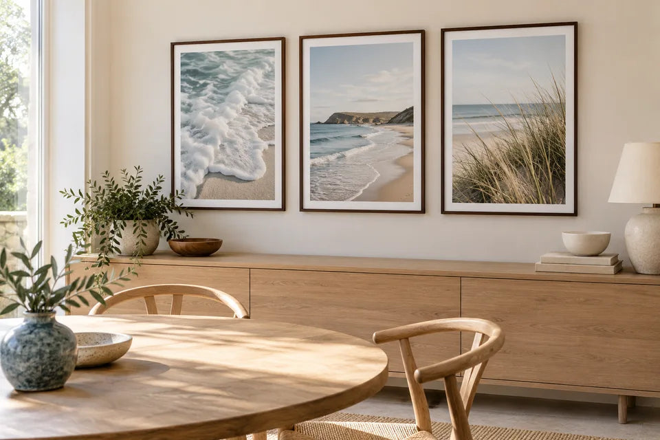 Three matching coastal paper posters displayed in slim dark frames in a bright dining space.