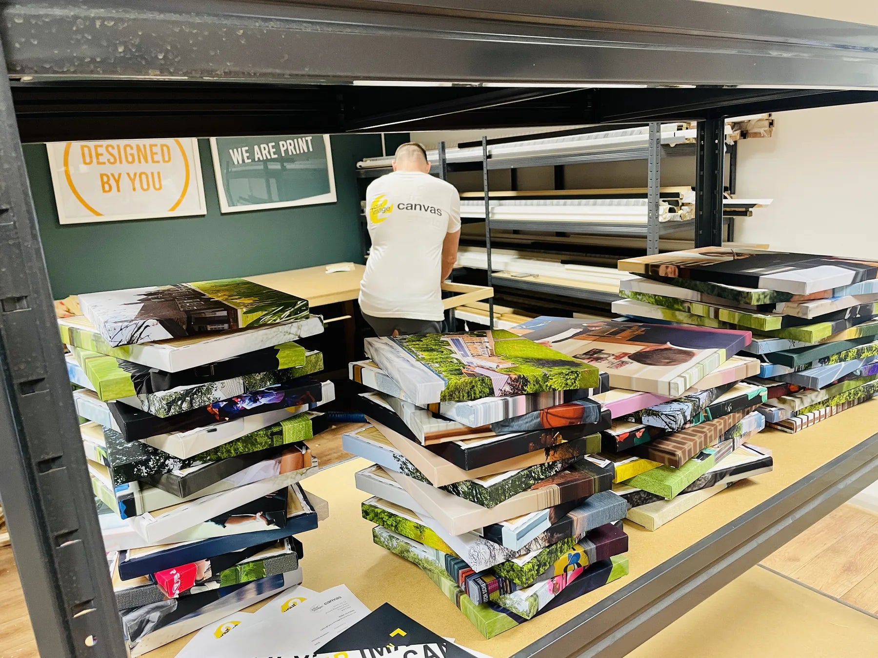 Workshop bench surrounded by tall stacks of completed canvas prints