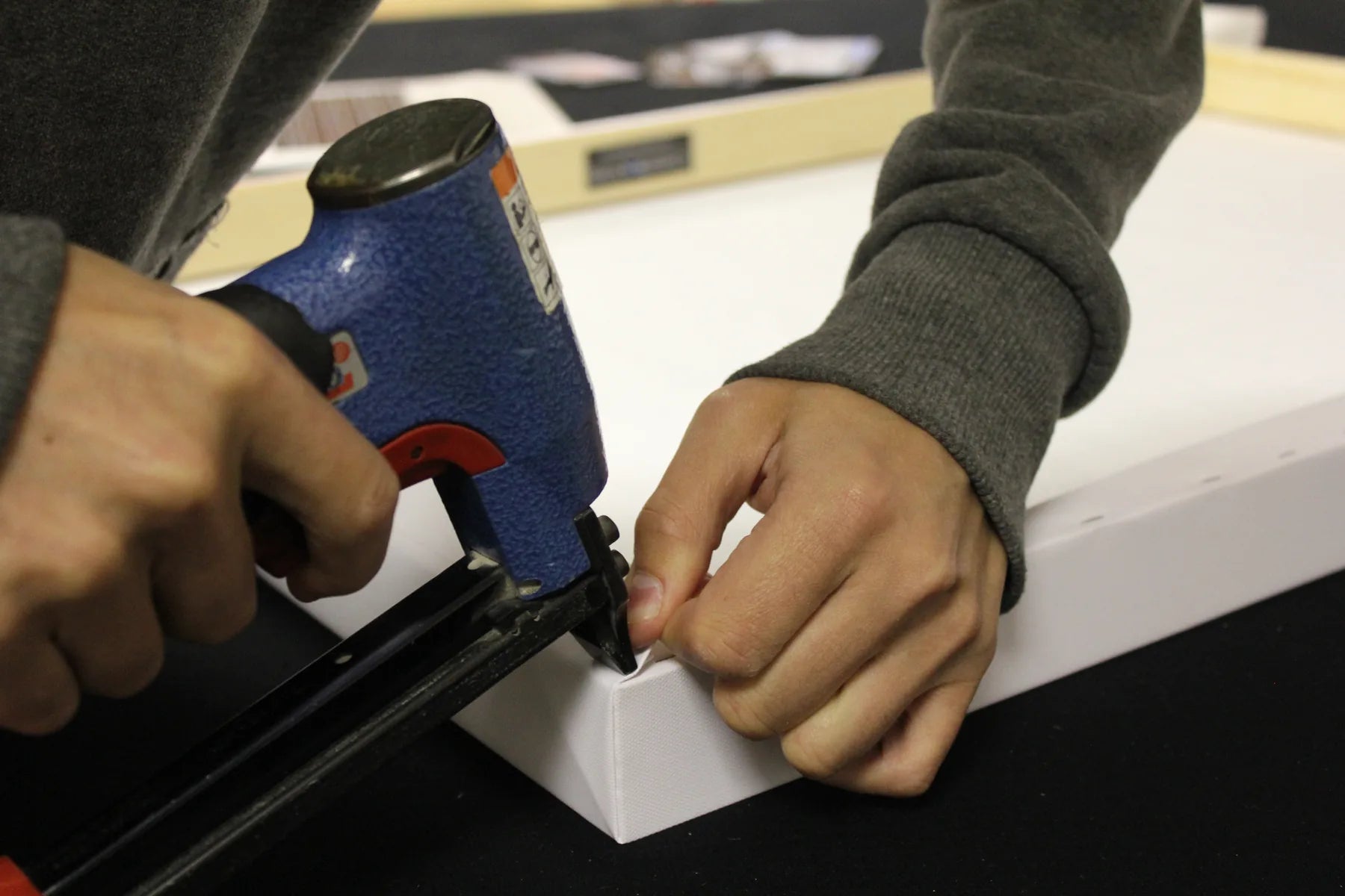 Close view of hands finishing a canvas neatly around a frame corner