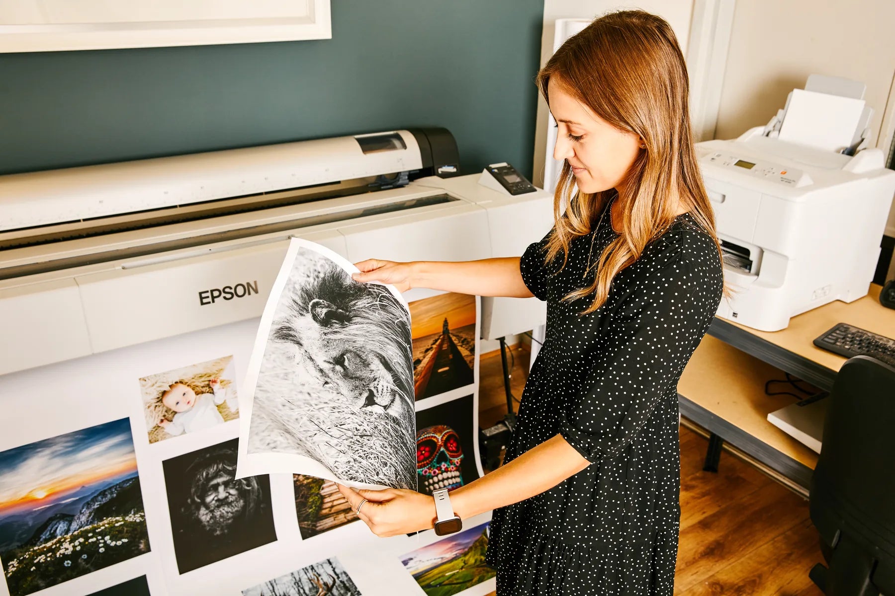 A printmaker comparing photographic prints beside a large-format printer
