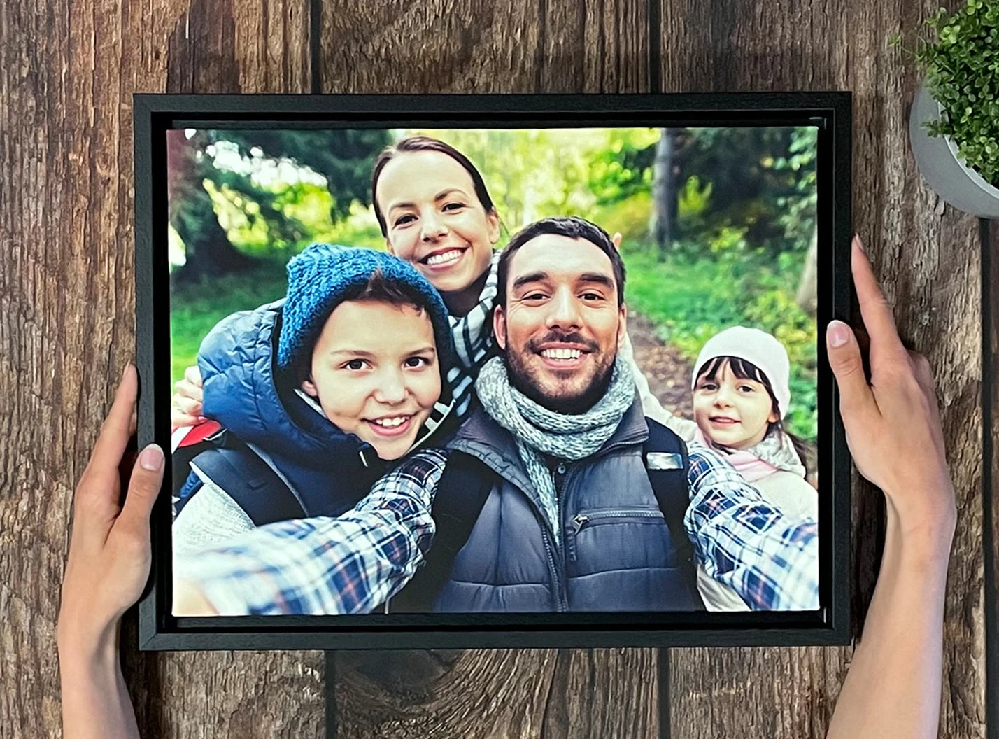 Finished product photograph showing the framed family print, hands, plant and wood background