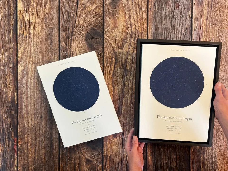A star map canvas and a star map in a black floating frame held over a wooden worktop.