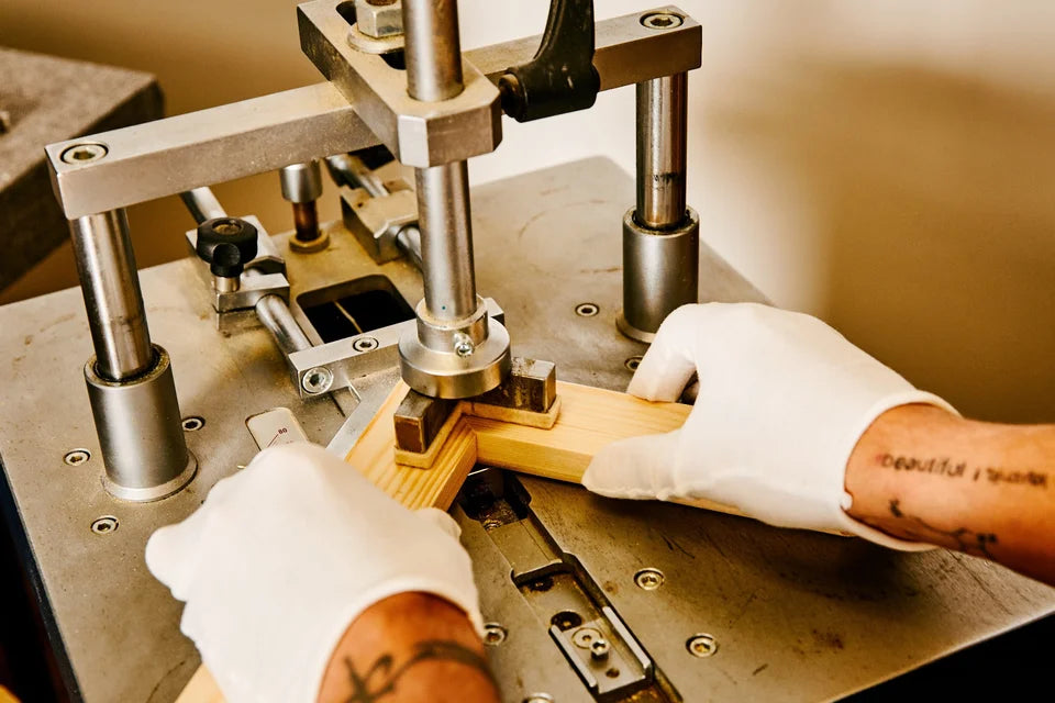 Gloved hands joining the mitred corner of a pine canvas support on the YI2C corner-pinning machine.