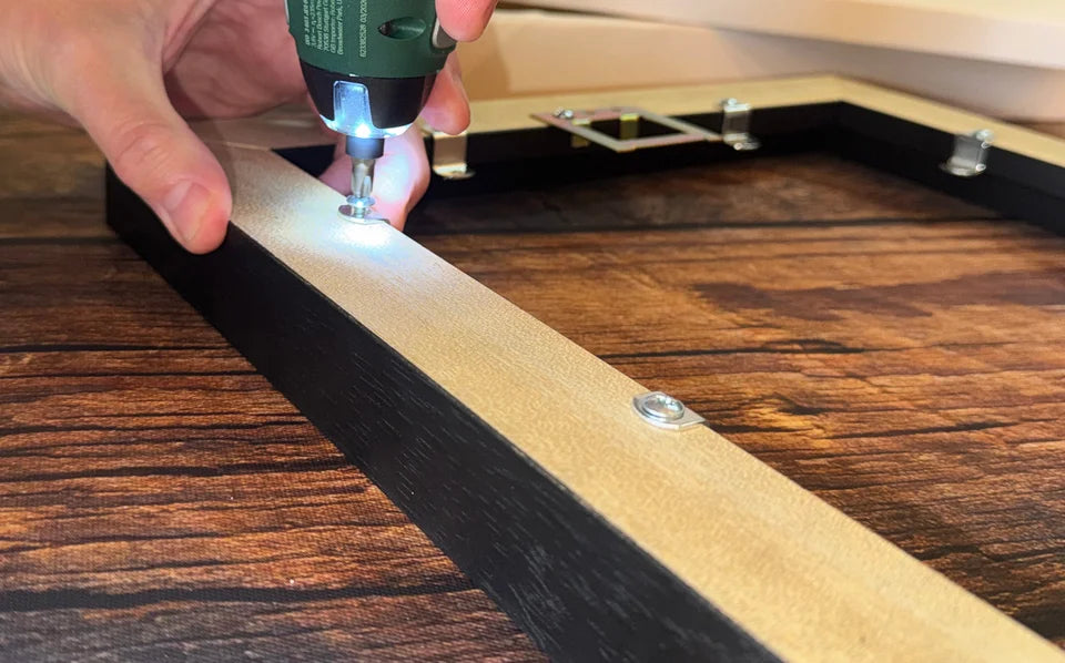 A YI2C team member using a screwdriver to secure the rear fixings of a black floating frame.