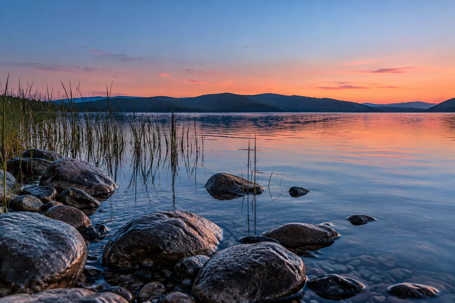 Illustrative lake scene after sunset, with foreground stones and reeds leading towards a softly coloured reflection.