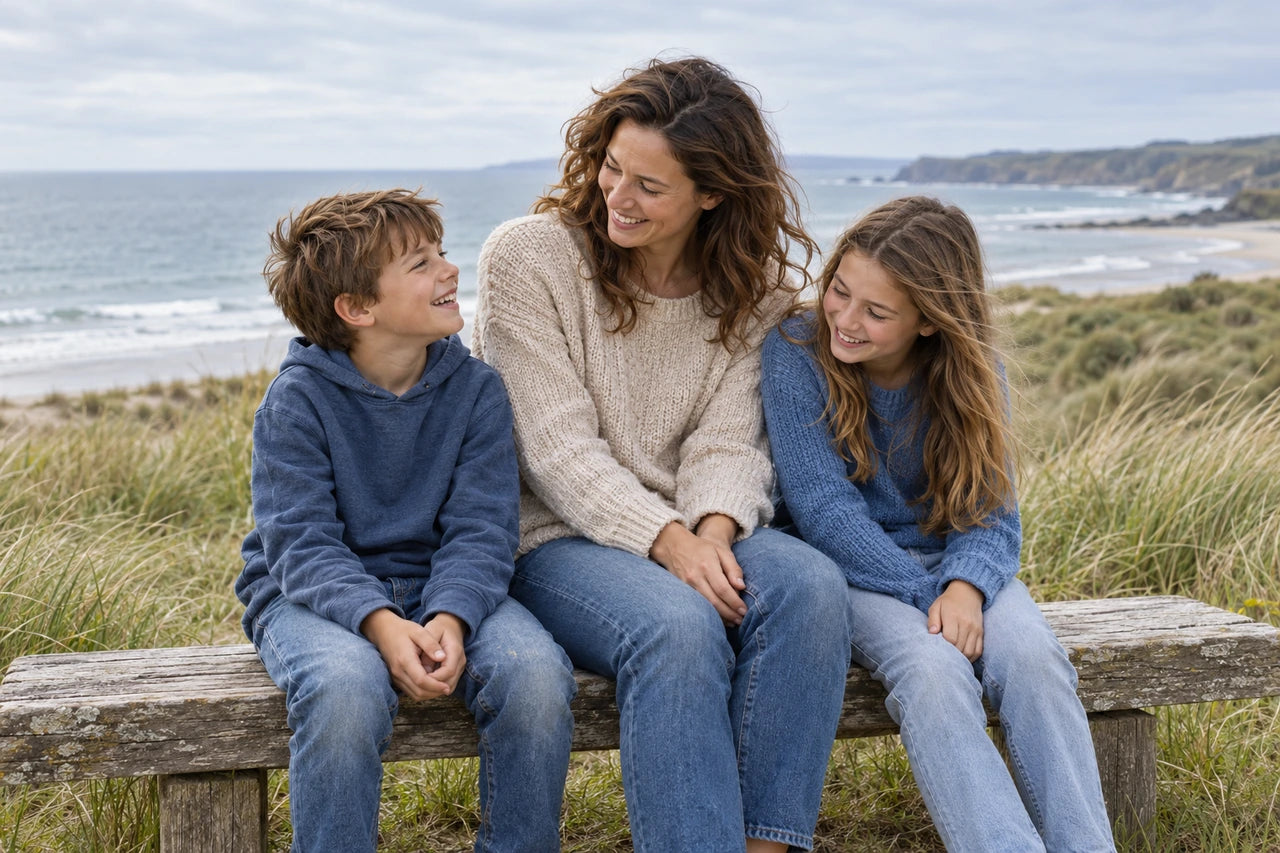 Fictional parent and two children smiling together on a coastal bench, with the group spread across a wide landscape composition.