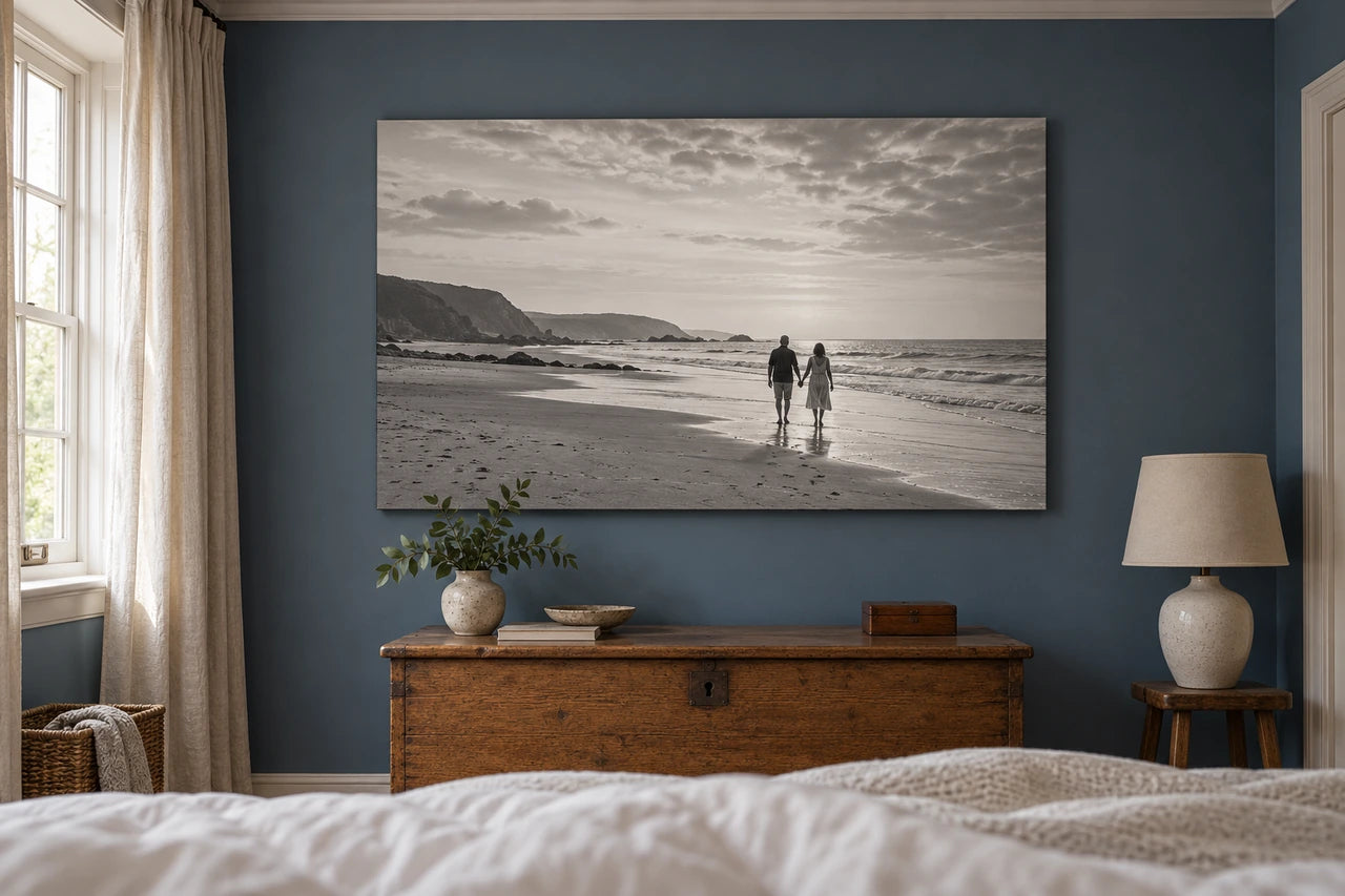 An imagined blue bedroom viewed from the bed towards a black-and-white canvas of two adults walking on a beach.