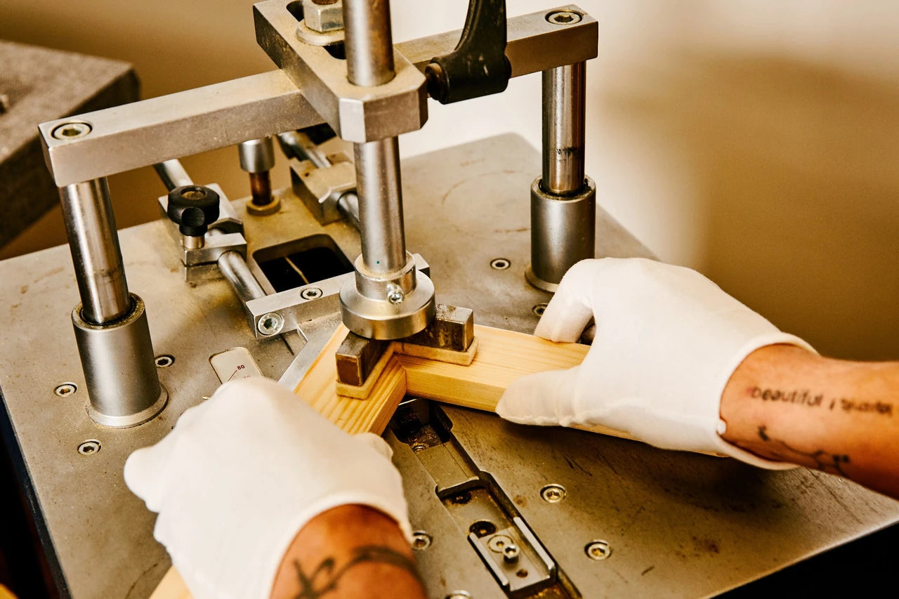Gloved hands joining a wooden canvas frame on a corner-pinning machine.