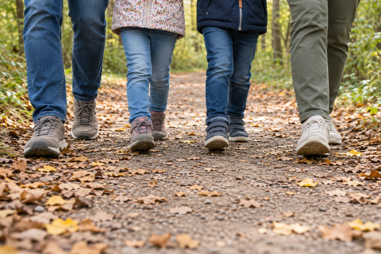 A low fictional view of family shoes and lower legs moving along a leaf-covered path.