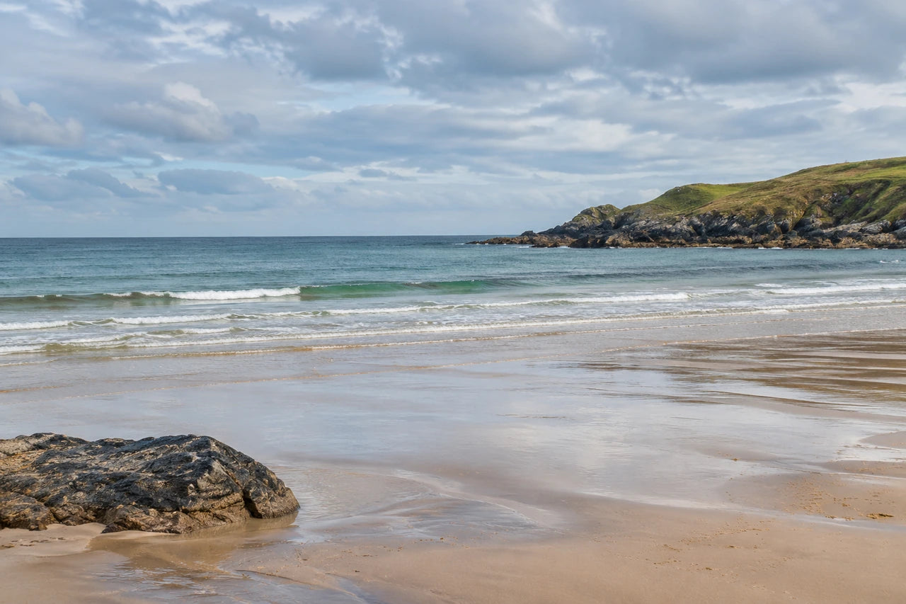 A fictional photographic-style British bay with wet sand, a dark foreground rock and grassy headland.