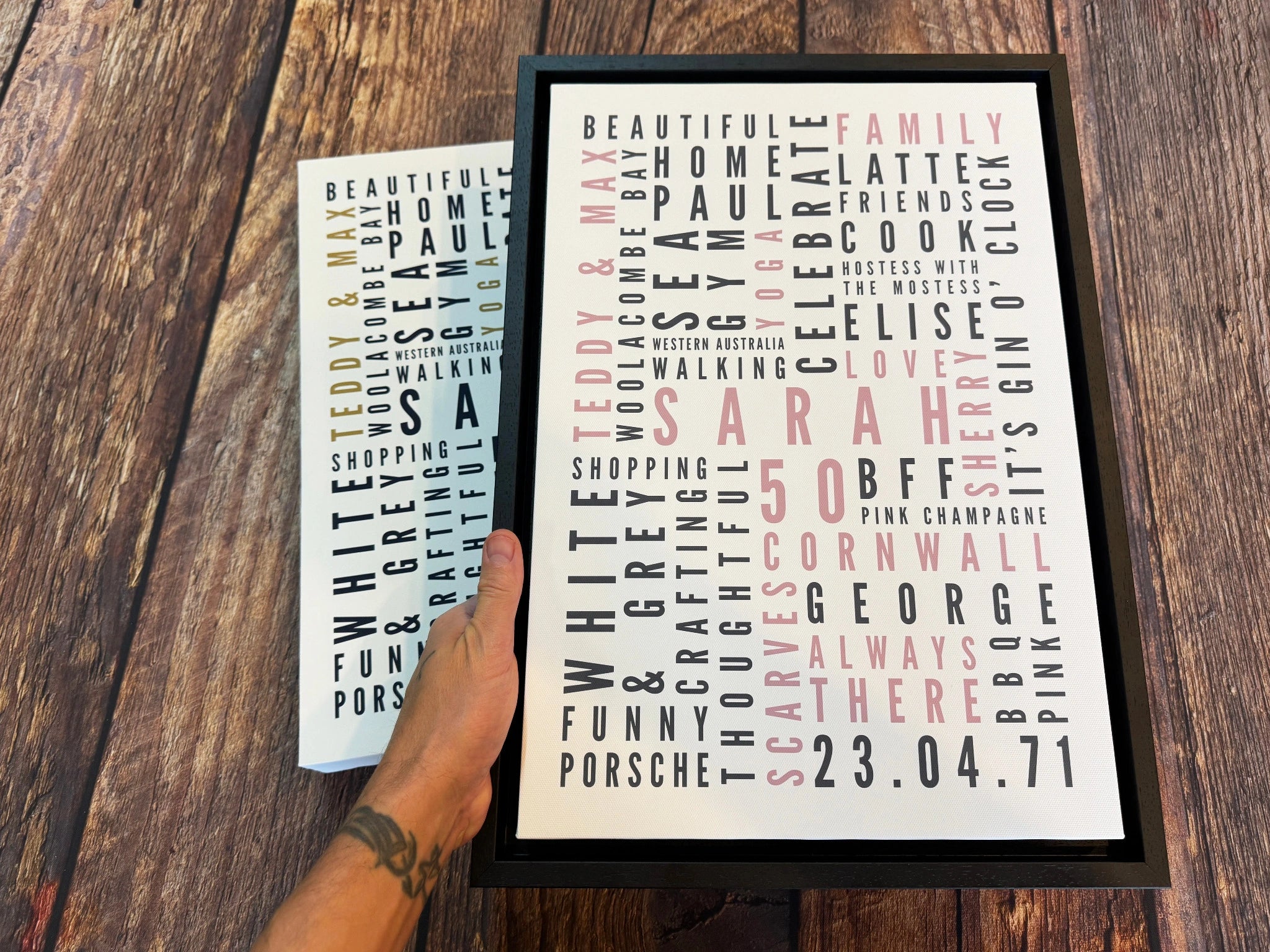 A personalised Word Art canvas in a black floating frame, held in front of a matching poster.