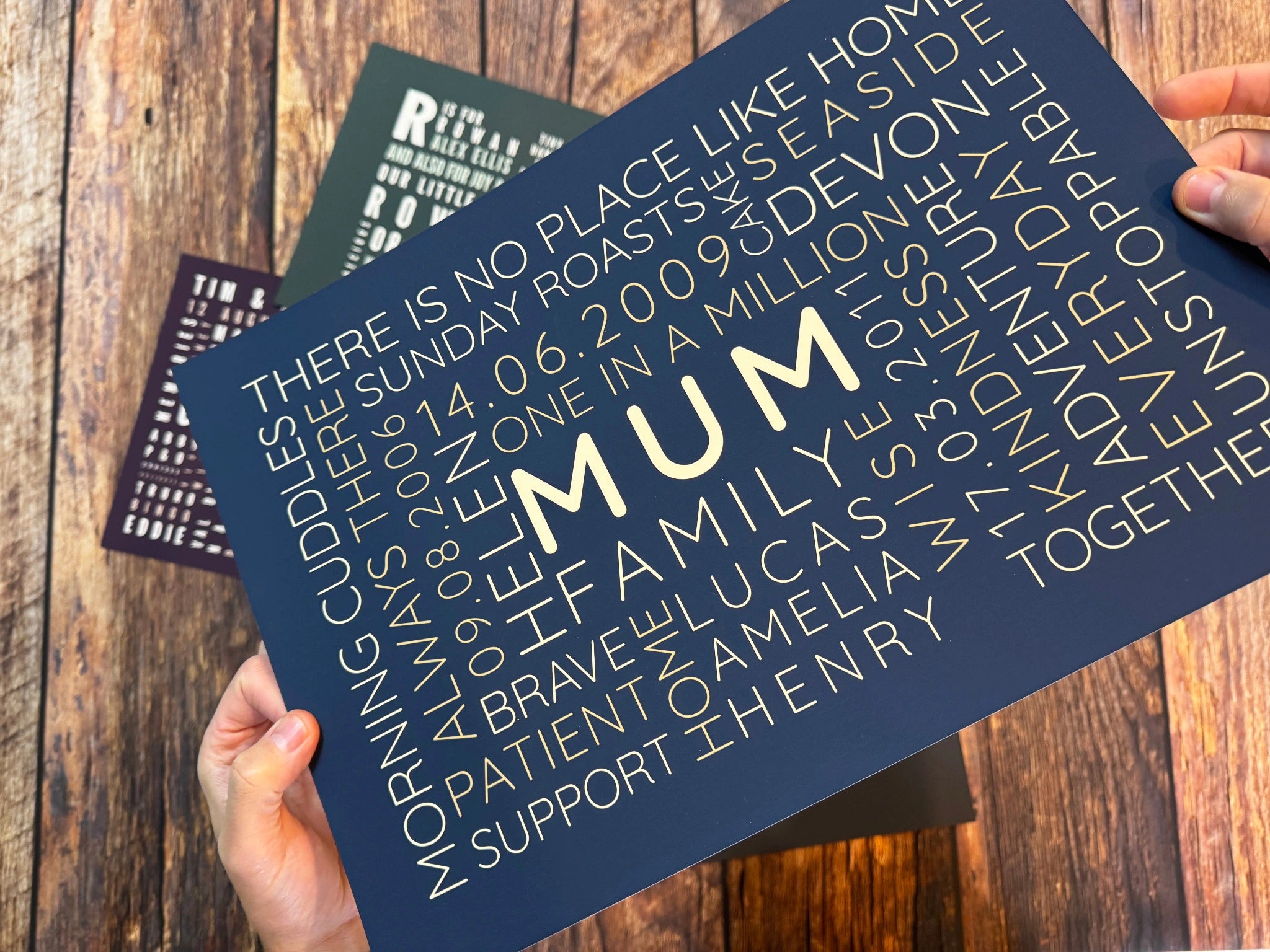 A navy and warm gold Mum Word Art poster held above a wooden worktop.