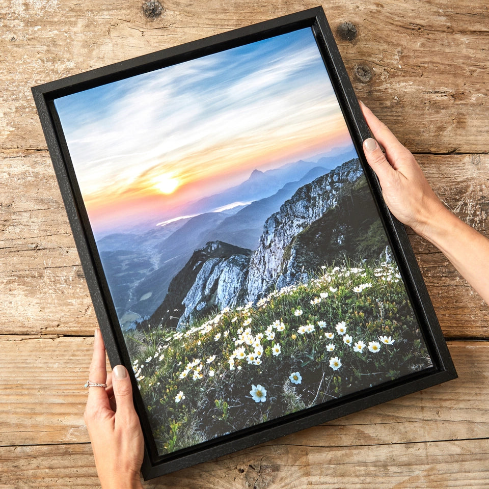 Hands holding a landscape canvas in a black floating frame