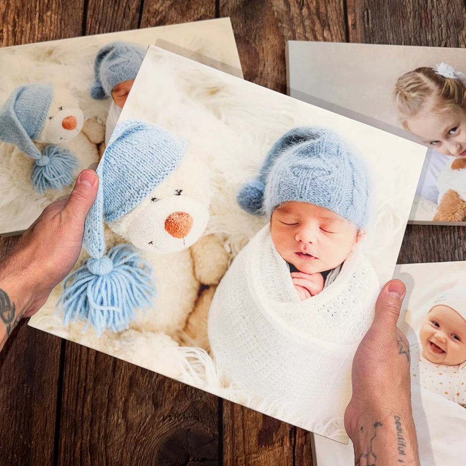 Hands holding a baby photo canvas above other finished canvases