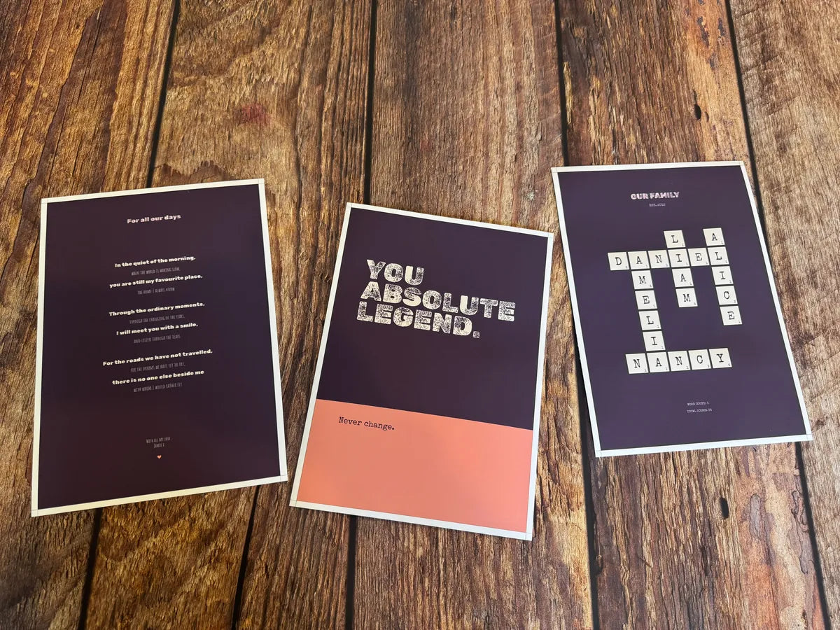 Three separate word-art prints on a wooden surface, sharing deep purple tones with one coral accent.