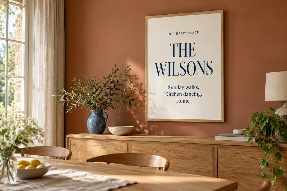 A family Word Art poster with personal phrases displayed in an oak frame in a warm dining room.