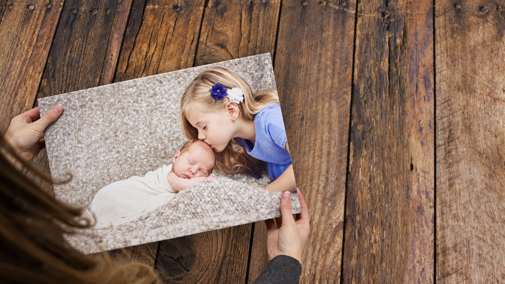 A finished family photo canvas showing a child kissing a newborn, held in both hands