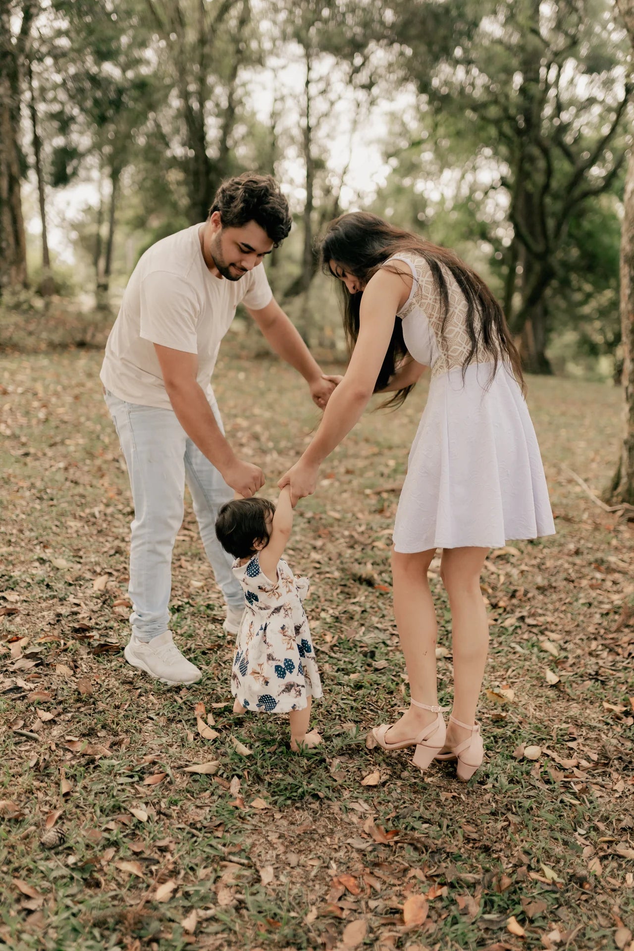 Original portrait photograph of two parents holding their child’s hands outdoors