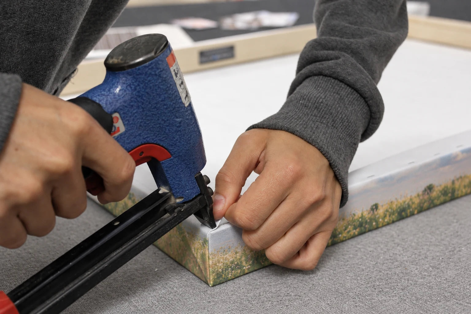 Hands stapling the family canvas around a pine stretcher frame