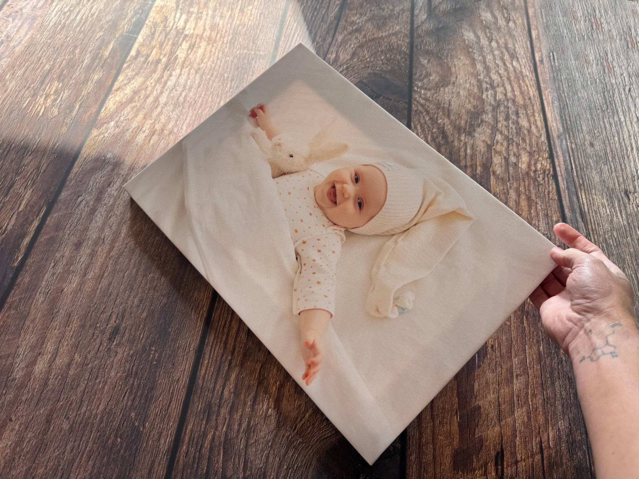 Hands holding a smiling baby canvas print above a wooden table.