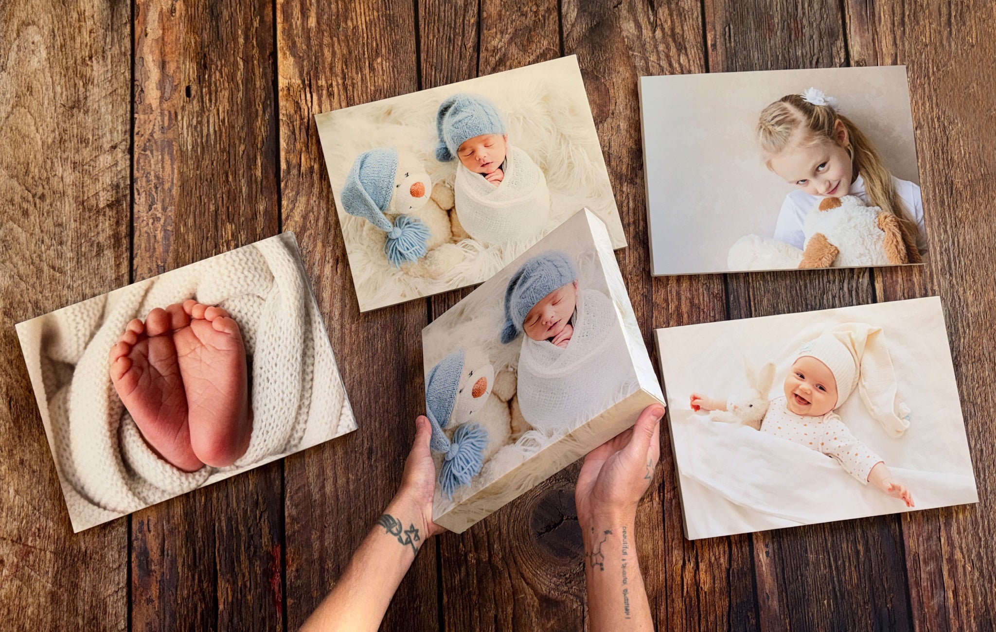 Baby and family canvas prints arranged on a wooden table, with one print held in the centre.