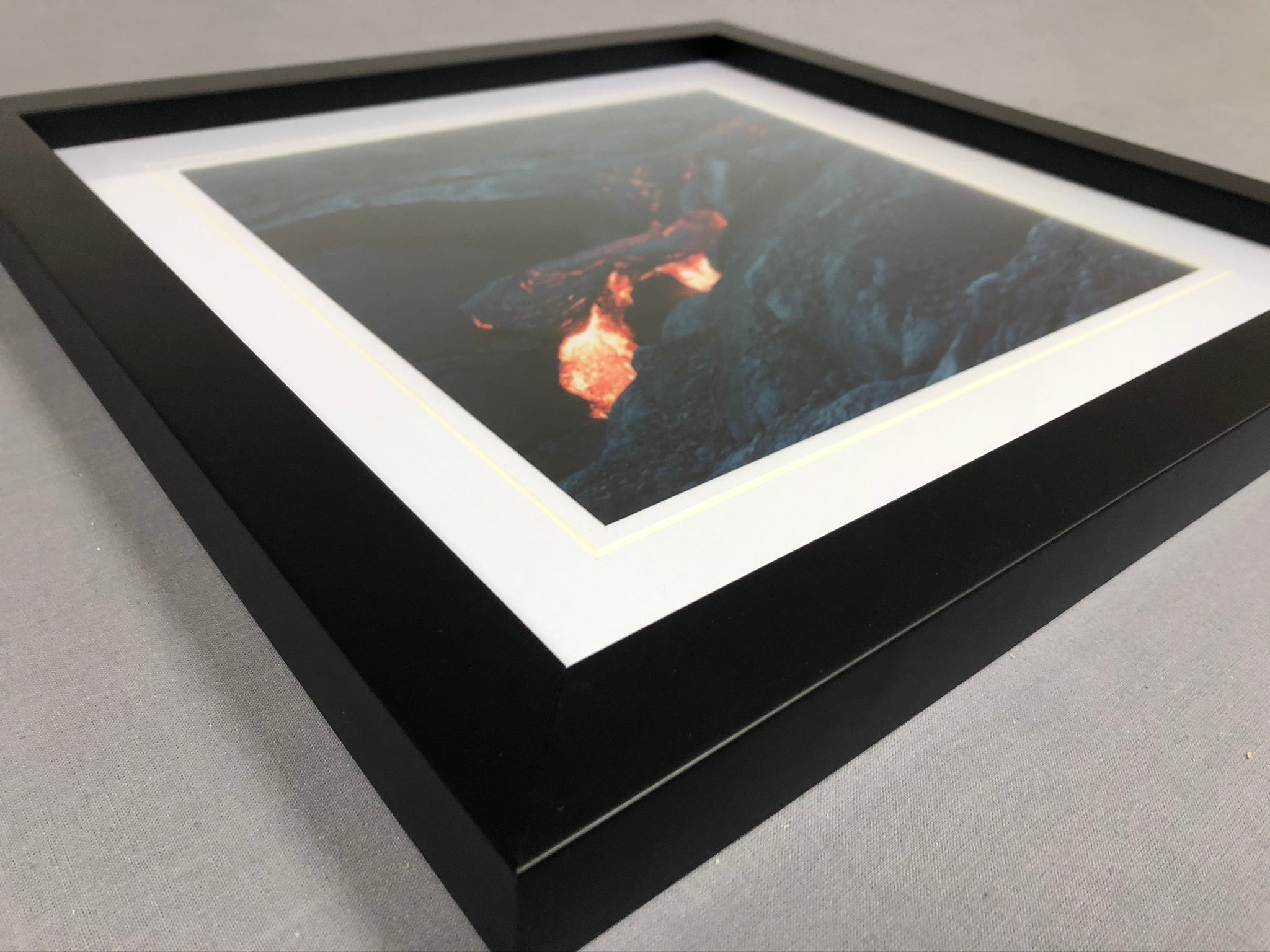 Close-up of a black picture frame, white mount and dramatic colour photograph against a plain grey background
