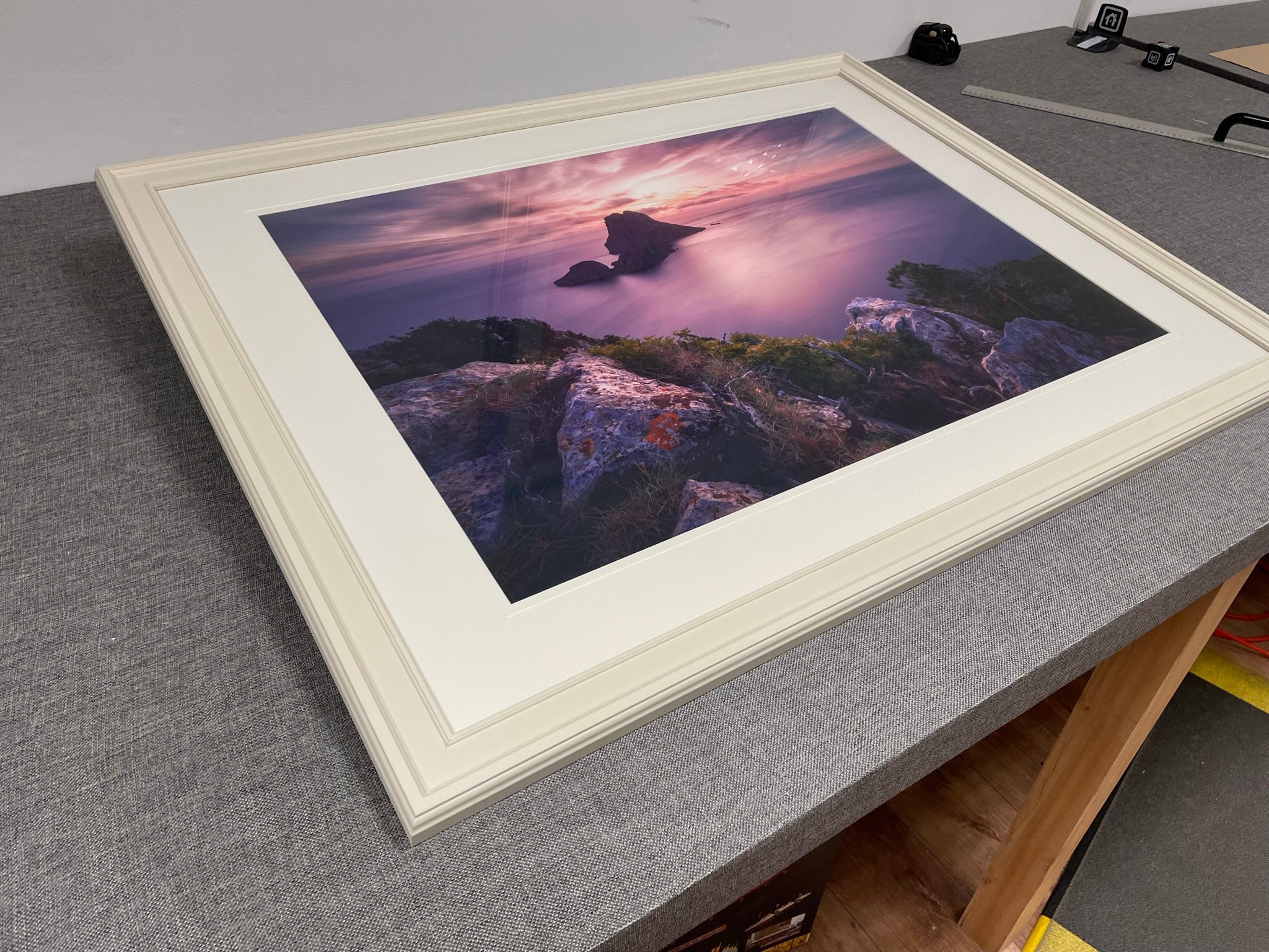 A coastal sunset photograph in a pale frame and white mount