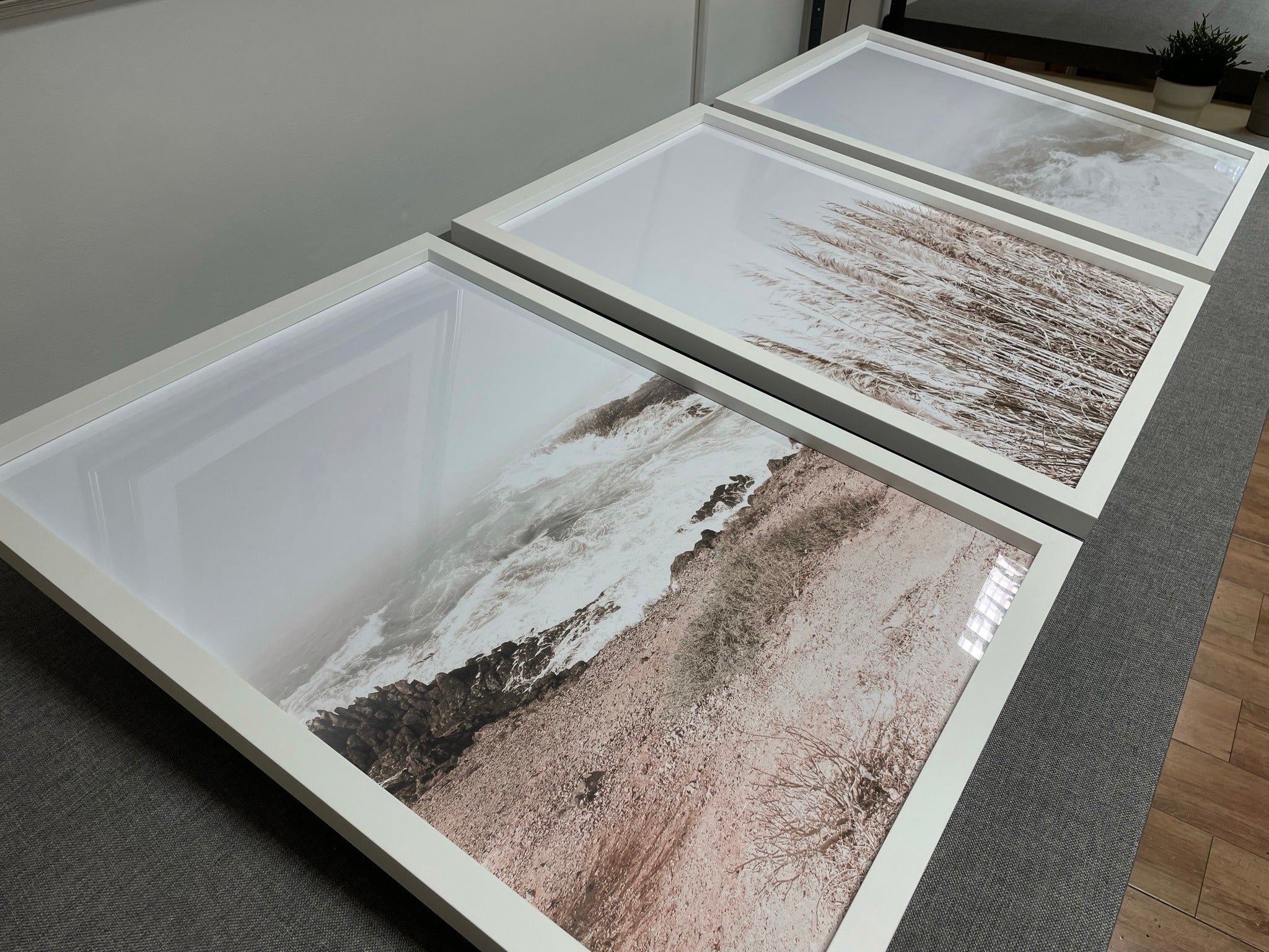 Three pale coastal prints in white frames on the workshop bench