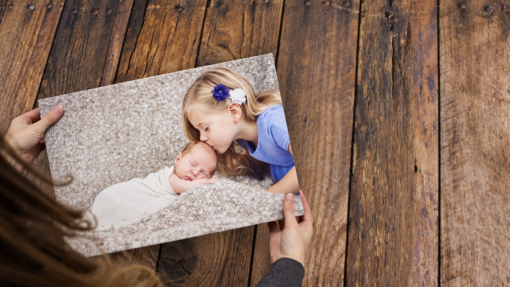A finished canvas showing a girl kissing her newborn sibling, held in two hands
