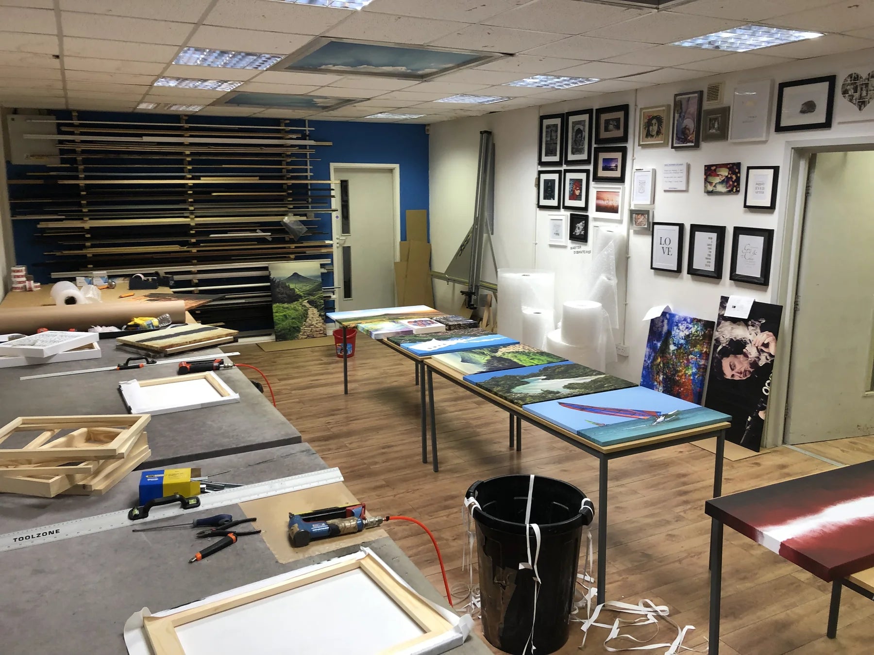 Wide view of an earlier working print room with frames and canvas prints on the benches