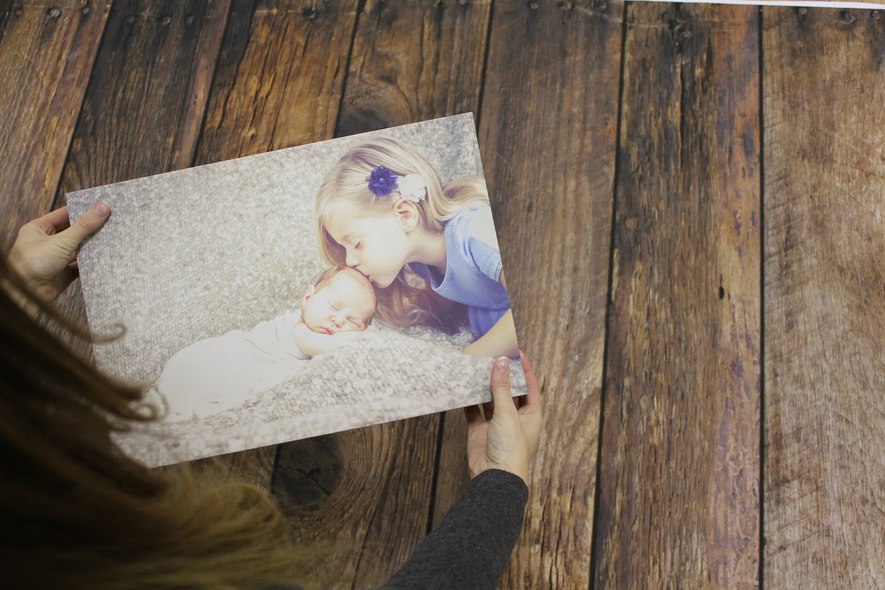 Hands holding a small baby canvas over the printed timber-floor background