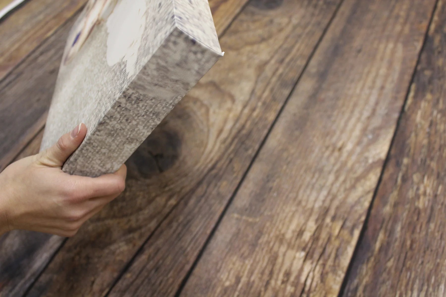 Hands lifting a textured baby canvas from the printed timber-floor background