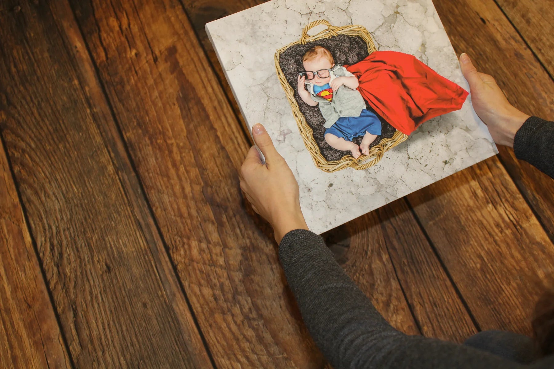 Hands holding a colourful child canvas over the printed timber-floor background