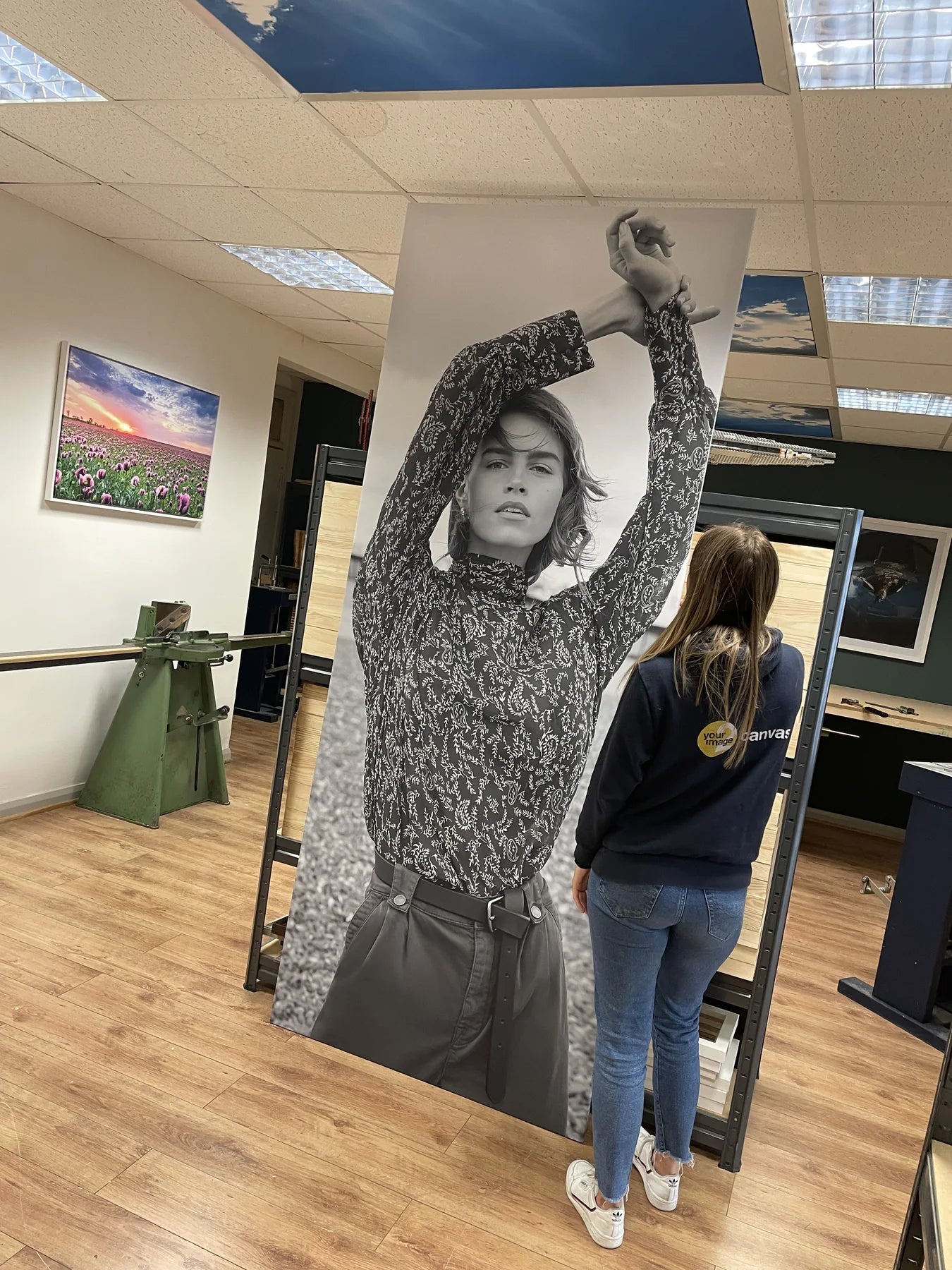 Two people carrying an extra-tall monochrome portrait canvas through the workshop