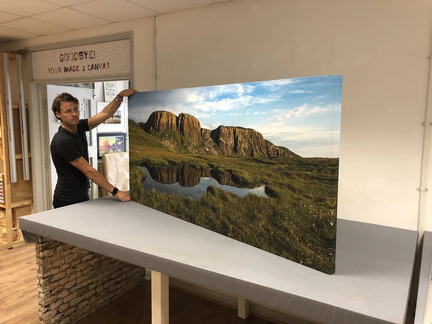 Printmaker standing beside a very large landscape canvas on a workshop table