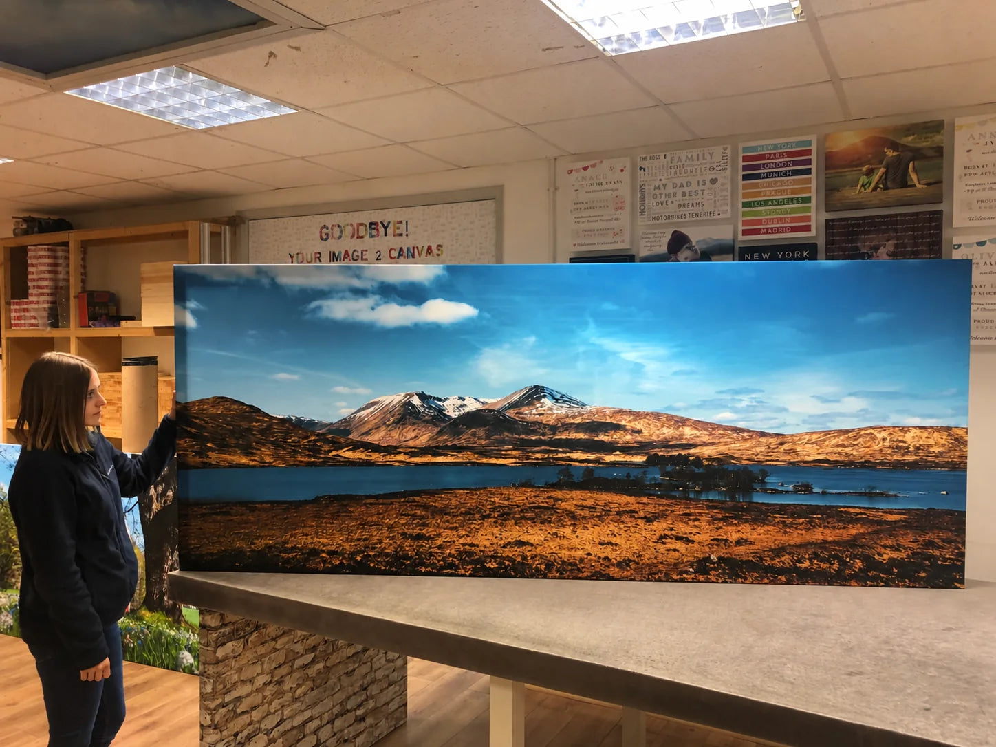 Woman checking a wide mountain panorama canvas in the workshop
