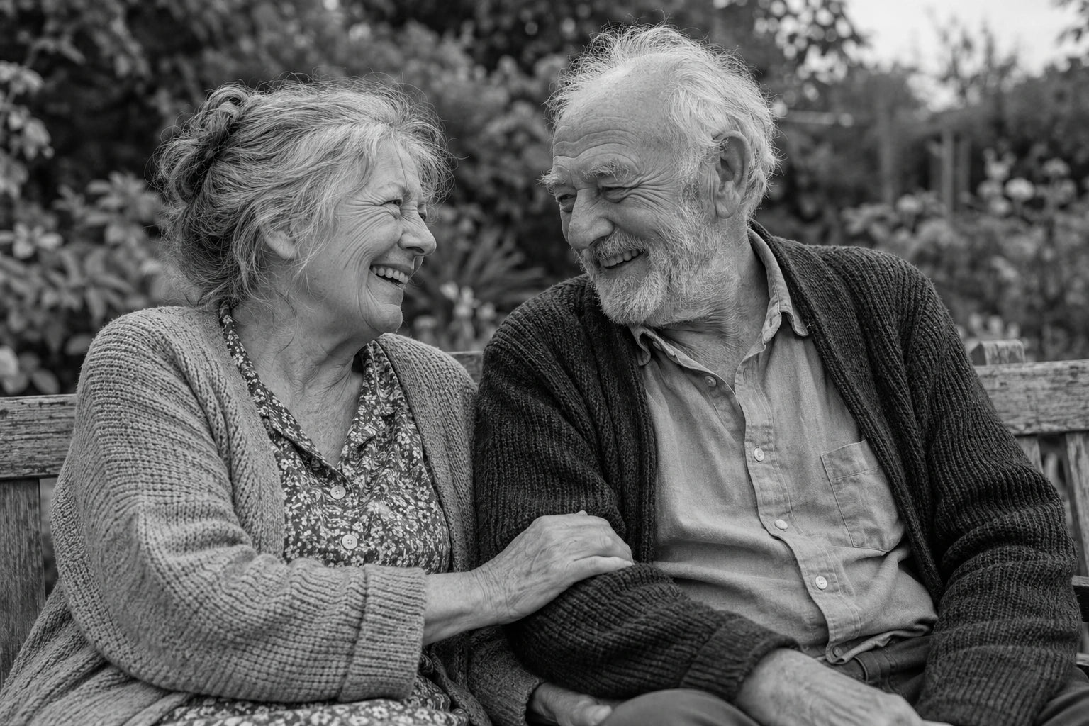 Two older adults sharing a spontaneous laugh on a garden bench, with natural expressions and relaxed clothing.