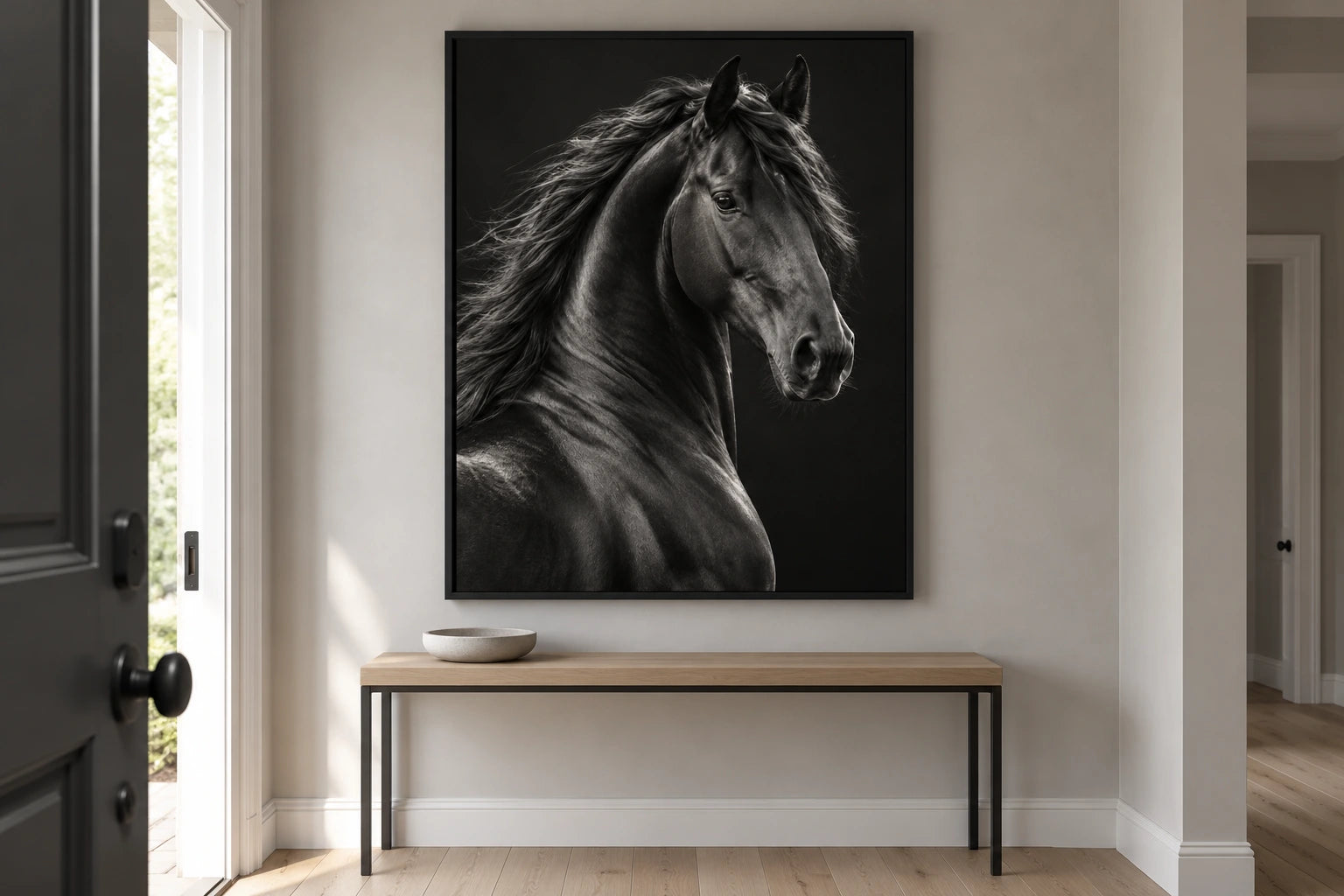 A large black-horse canvas in a black floating frame above a simple console in a pale entrance hallway.