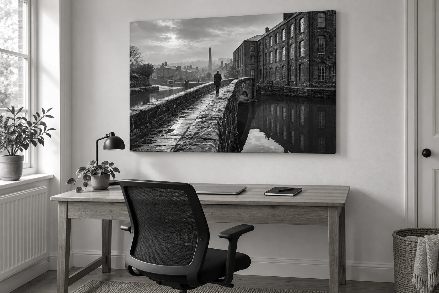 An imagined working-town photograph shown as a landscape canvas above an oak desk in a home office, photographed in black and white.