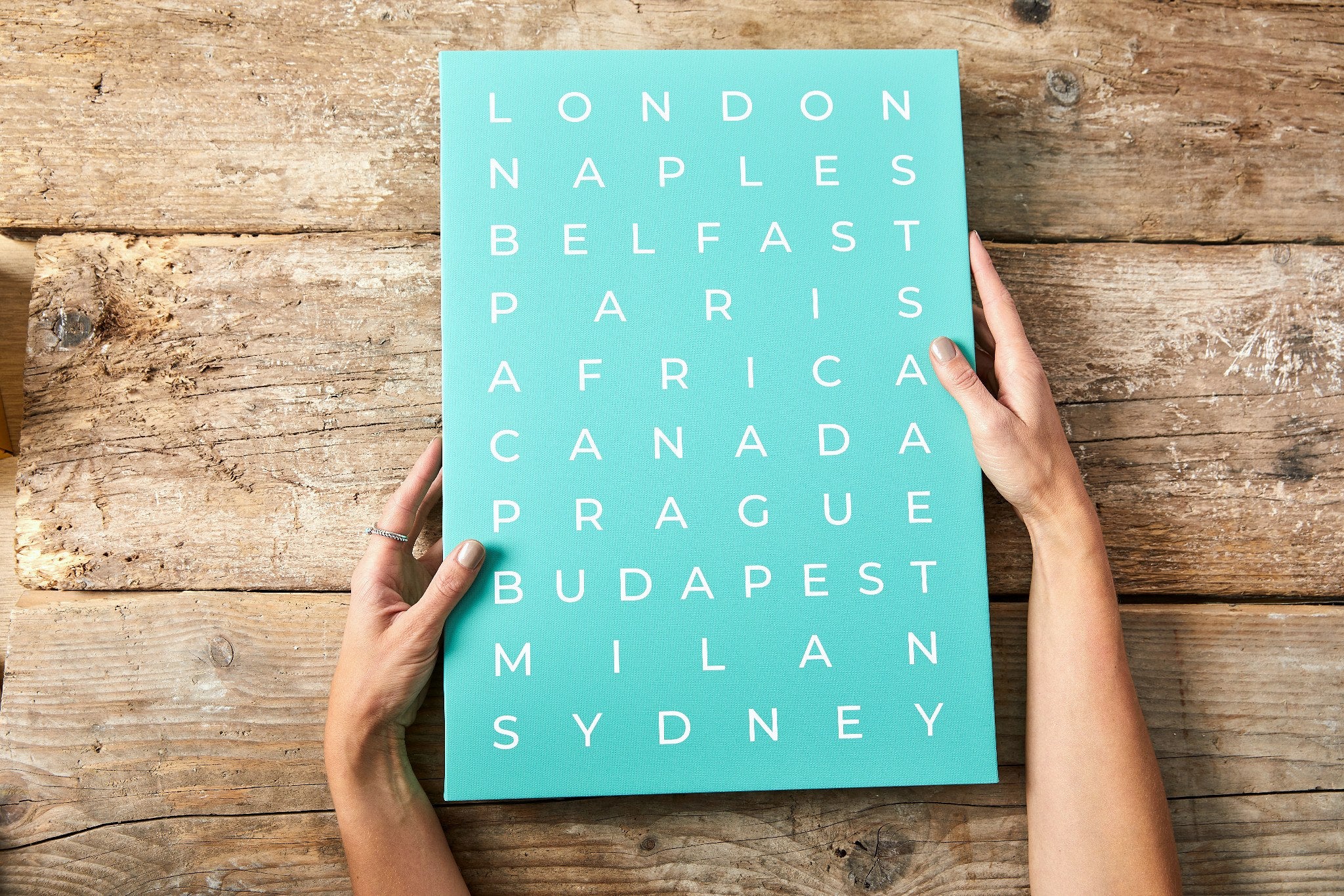 Hands holding a turquoise typographic canvas