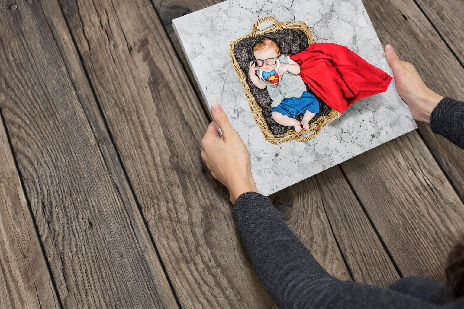 Hands holding a finished superhero baby canvas on a wooden table