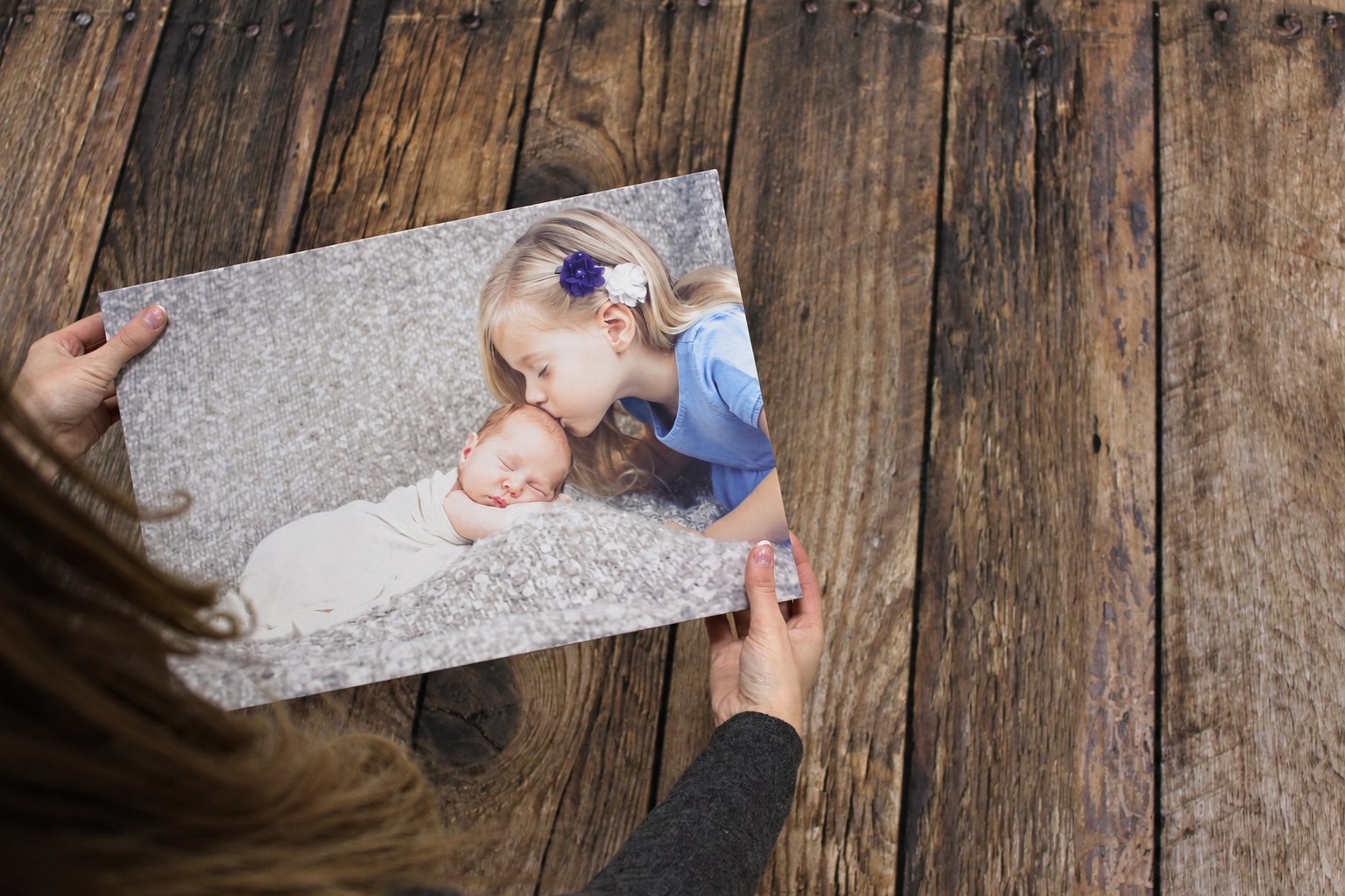 Hands holding a finished canvas of a child kissing a newborn