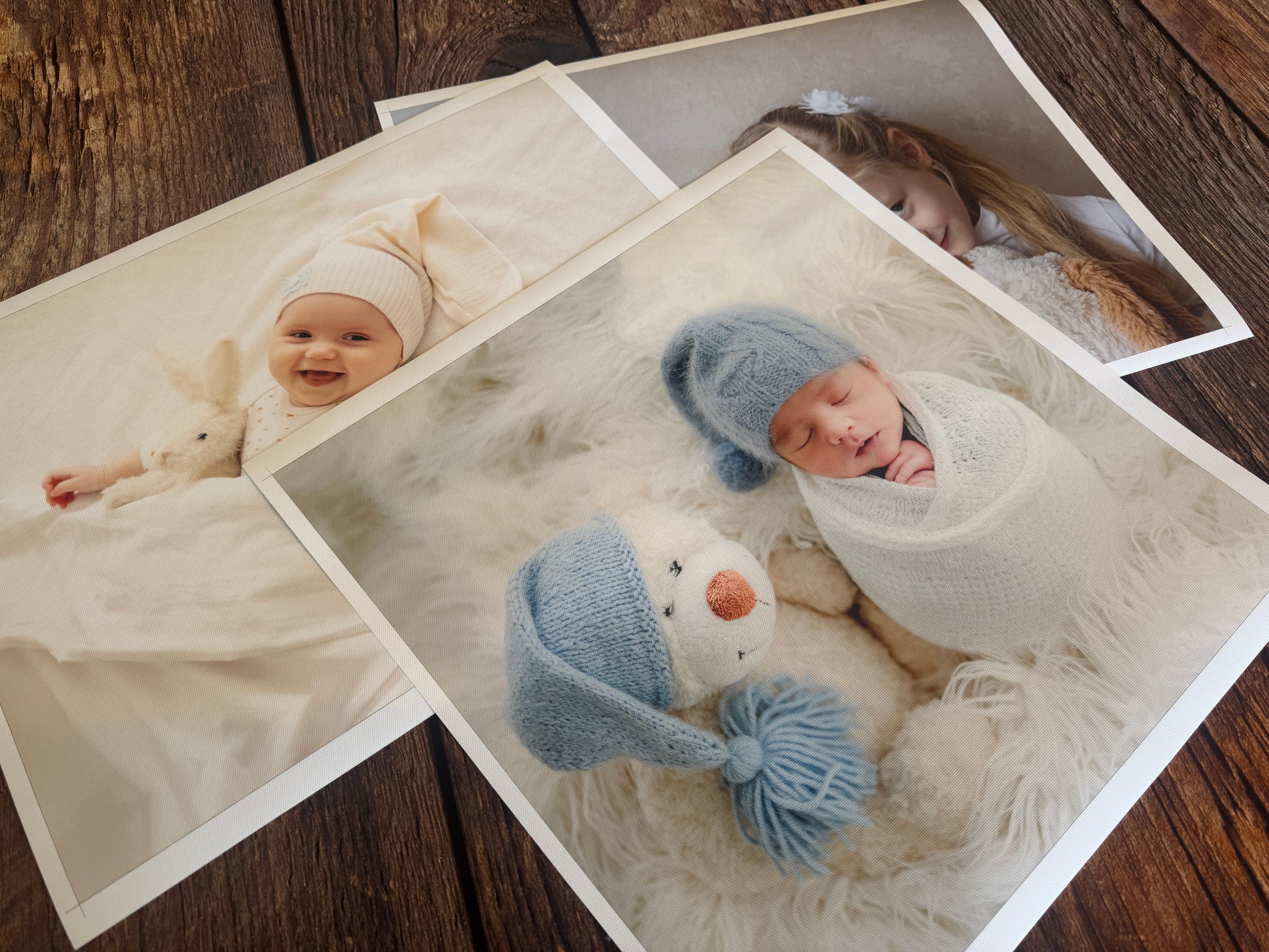 Unstretched canvas sheets printed with baby and family photographs on a wooden table.
