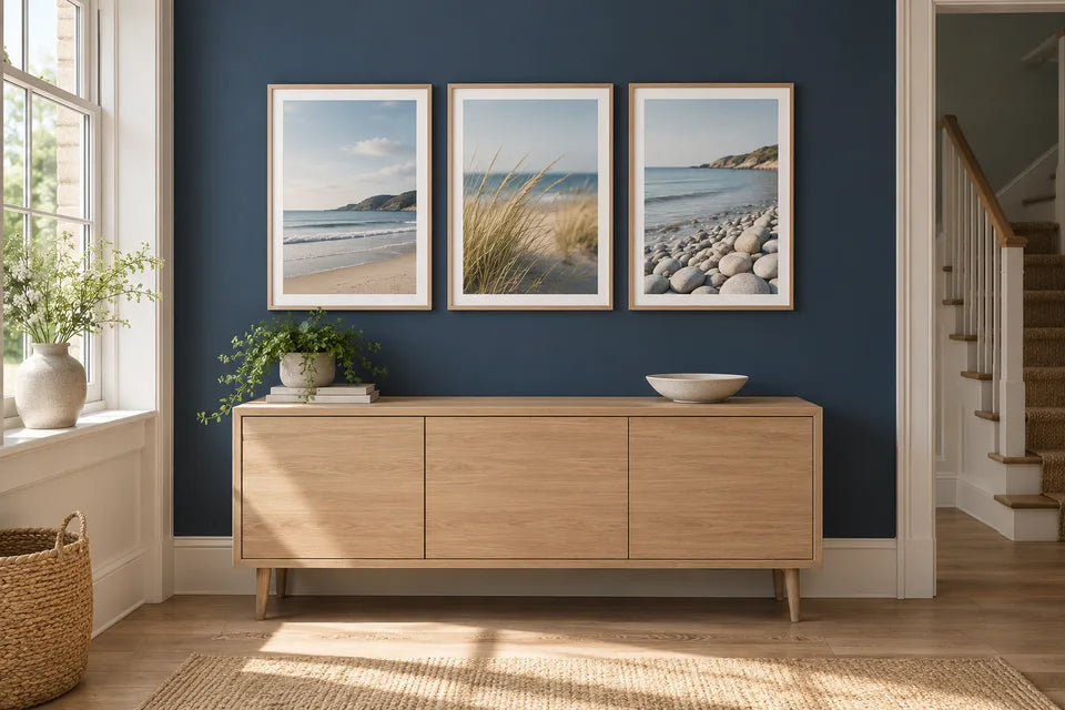 Three coordinated coastal photo posters in light wood frames above a navy hallway sideboard.