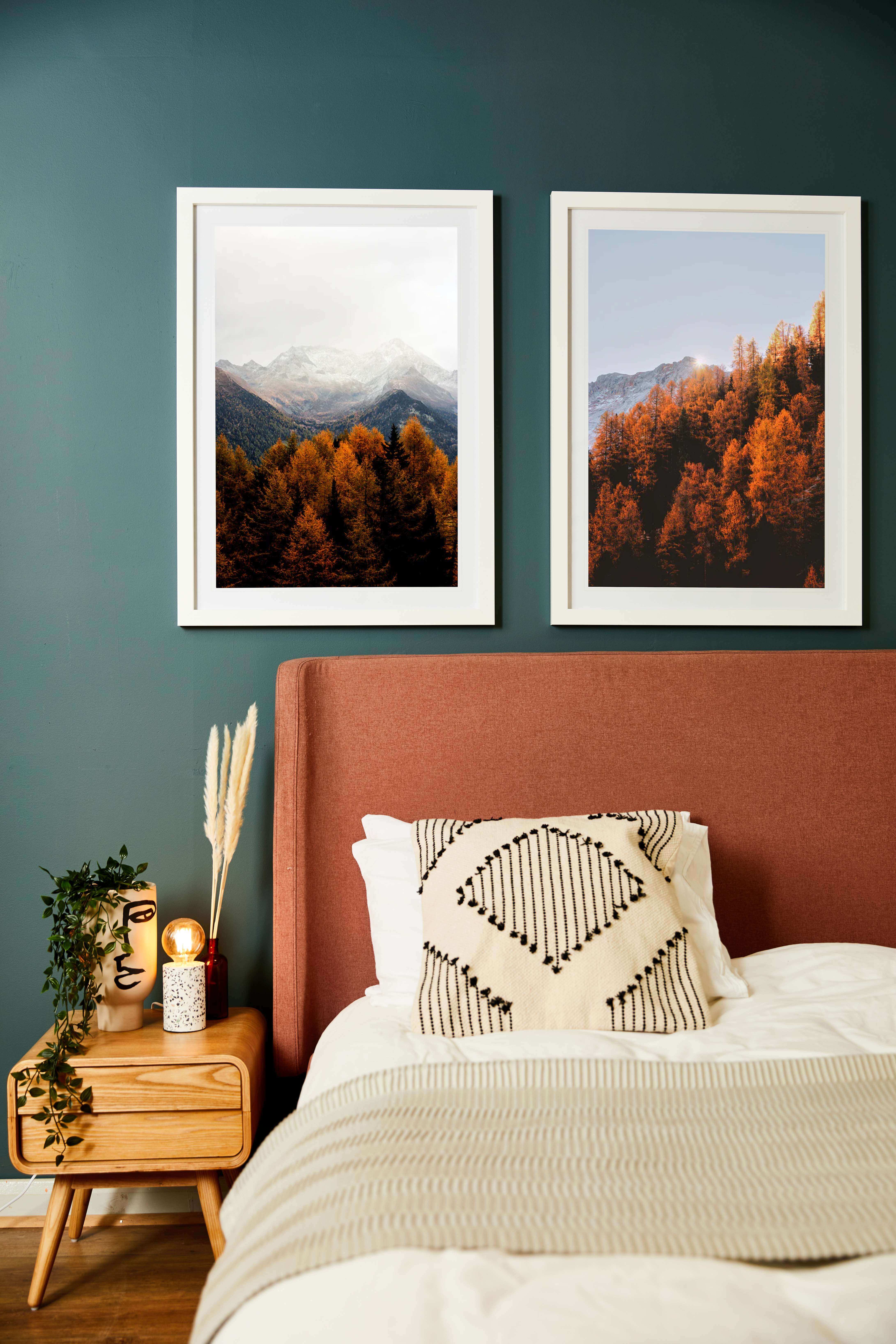 A photograph of two autumn nature shots printed onto quality canvas and displayed in beautiful white picture frames in a bedroom